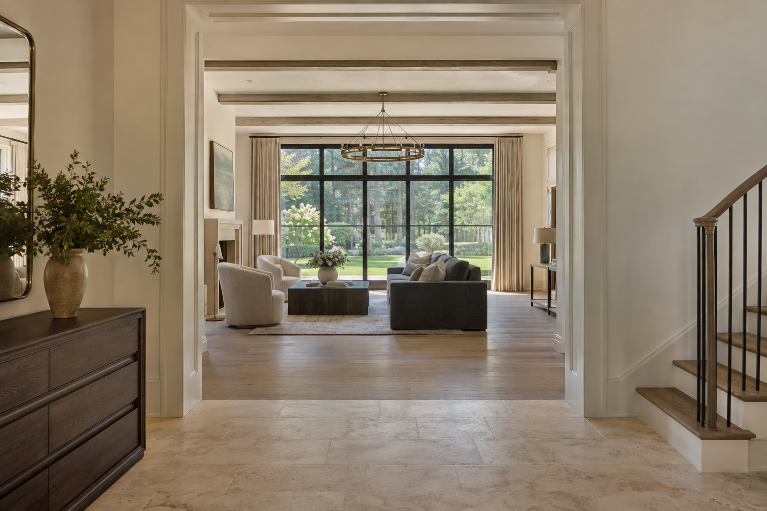 A limestone entry gallery opens to a white oak living room with dark-framed windows overlooking a flat lawn and mature Piedmont trees.