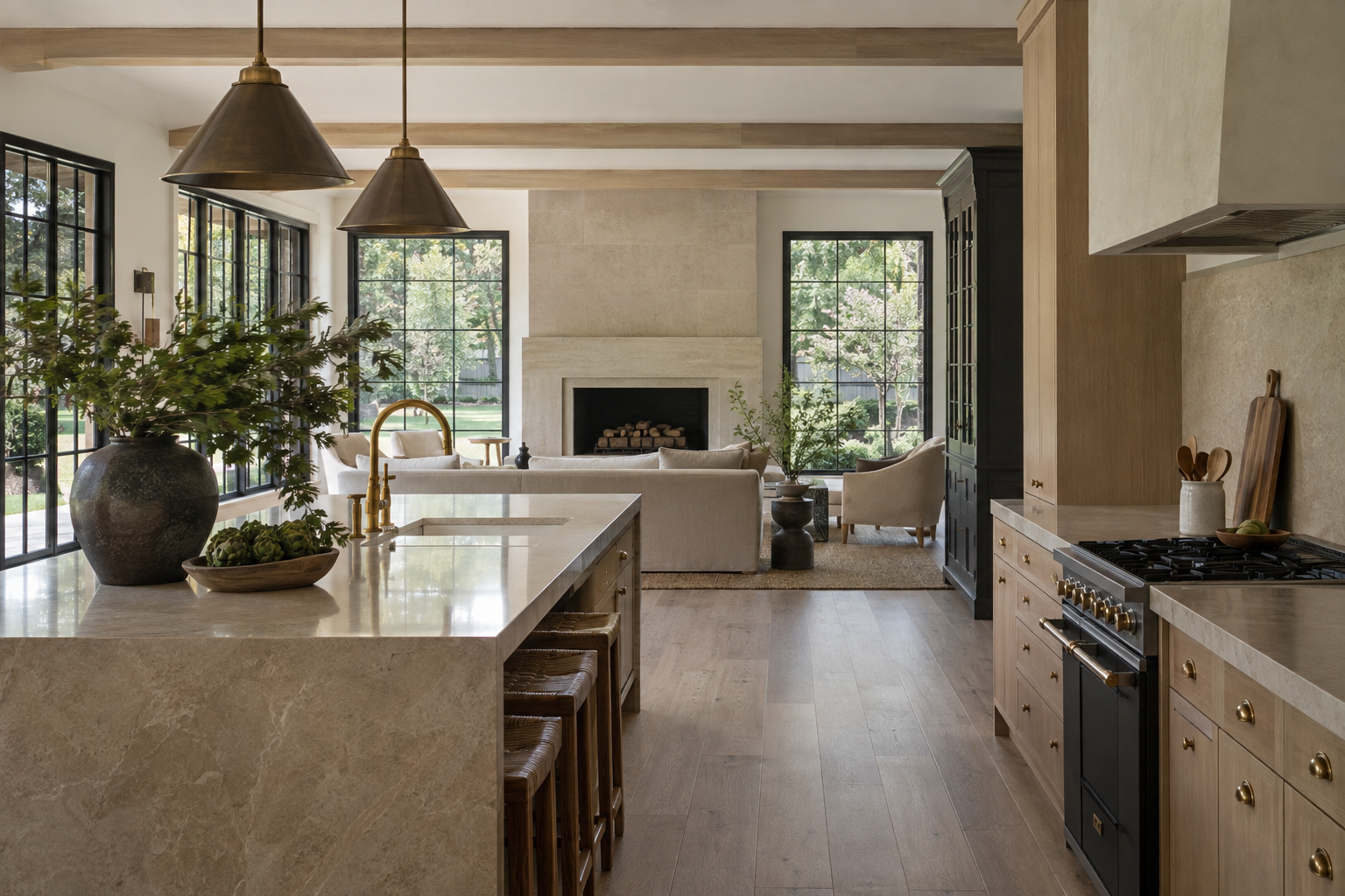 A white oak and limestone kitchen opens to a living room with a limestone fireplace and windows overlooking a flat, tree-lined lawn.